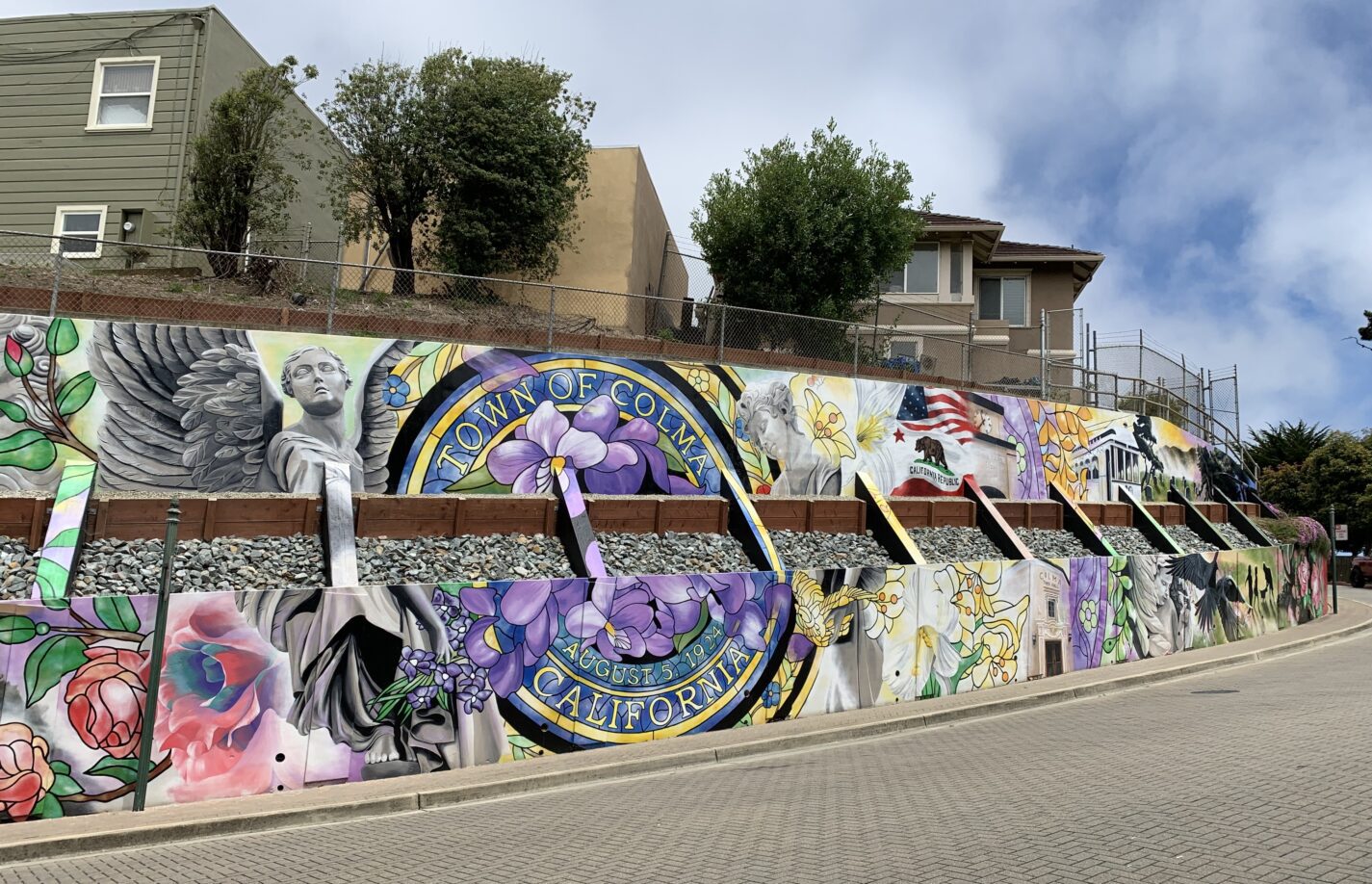 Colorful mural representing the Town of Colma including flowers and statues and a streetcar